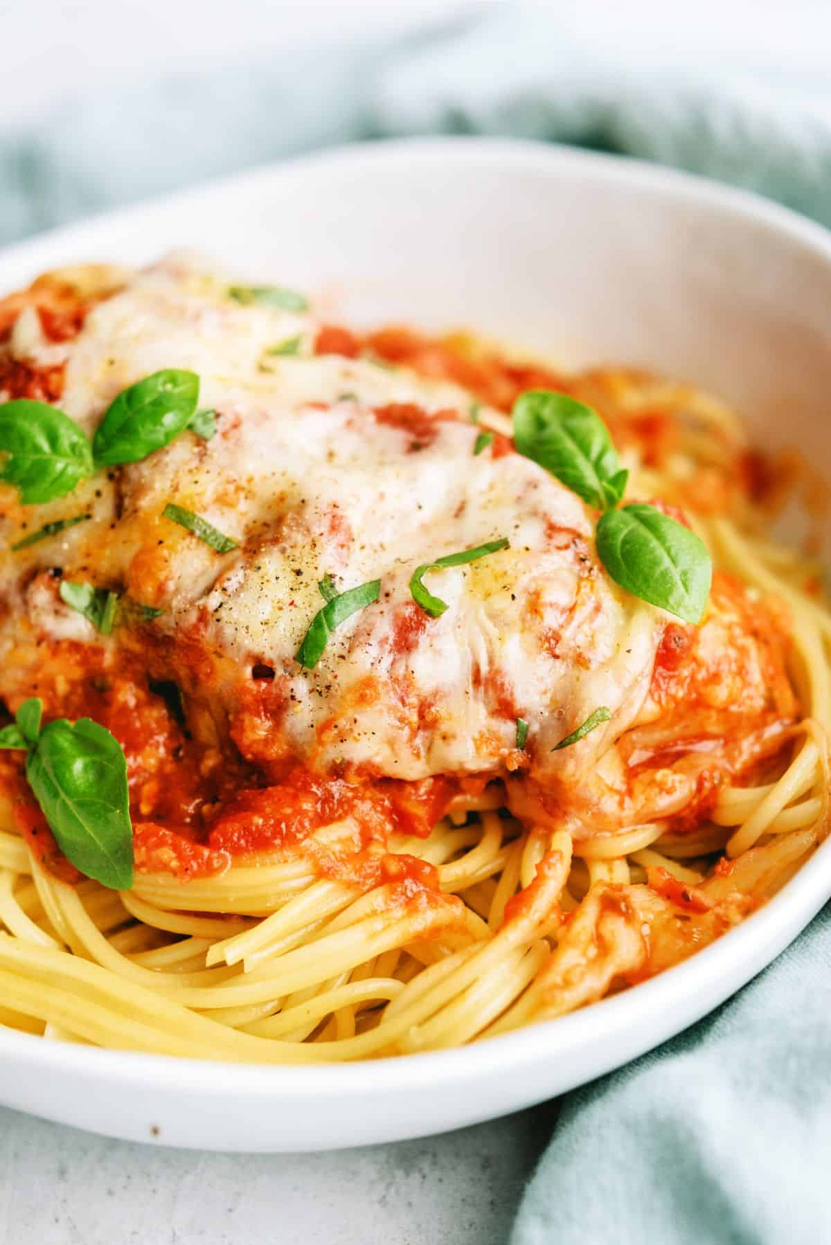 Close up of Slow Cooker Chicken Parmesan served in a bowl on top of spaghetti noodles