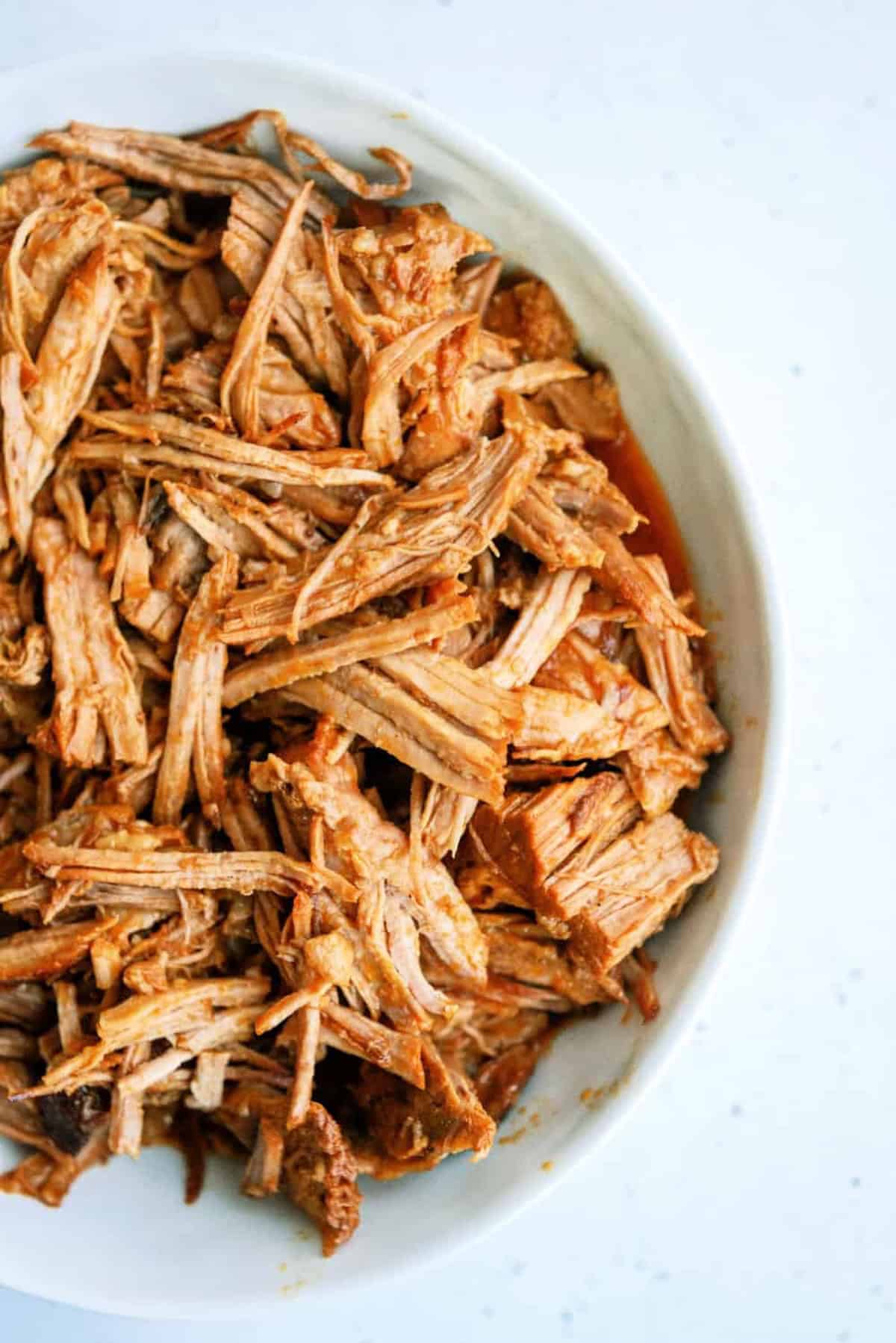 A white bowl filled with shredded, seasoned cooked meat on a light surface.