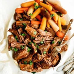 Tender beef pot roast with carrots and potatoes, served on a white platter.