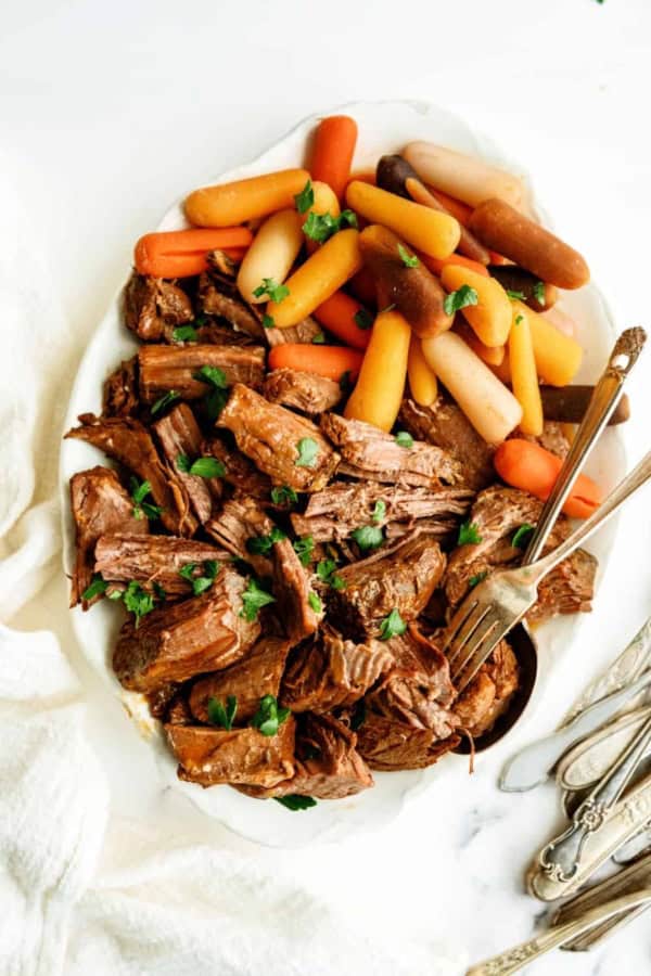 Tender beef pot roast with carrots and potatoes, served on a white platter.