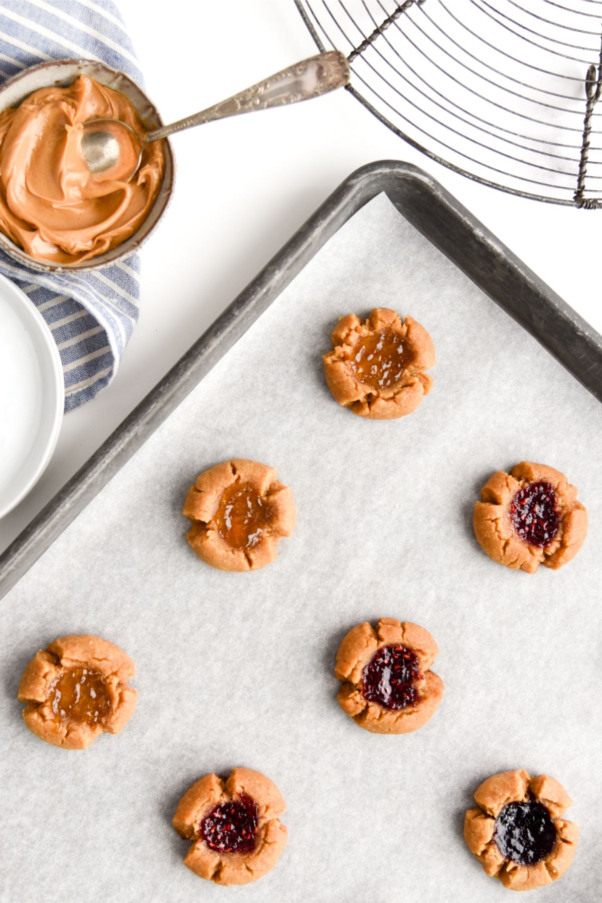 5 Ingredient Peanut Butter and Jam Thumbprint Cookies on a pan lined with parchment paper with peanut butter on the side