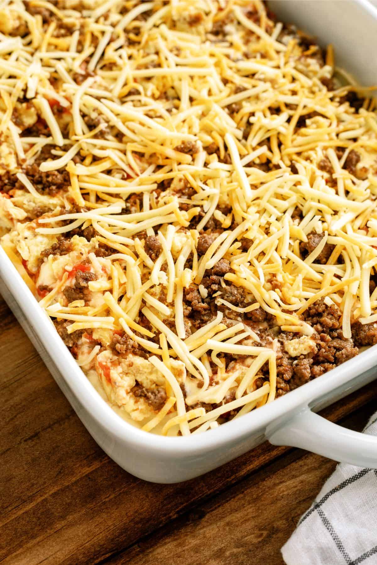 A white baking dish filled with a layered casserole topped with shredded cheese, ground meat, and visible layers of vegetables and sauce.