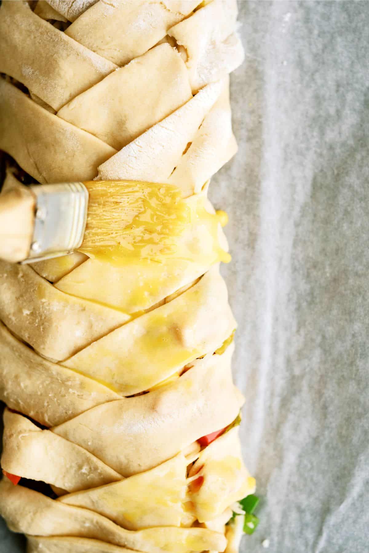 Brushing egg wash onto the Cheesesteak Crescent Braid