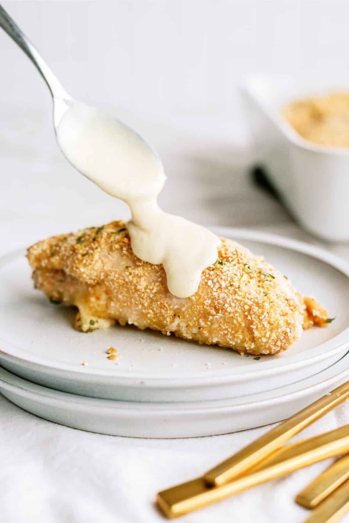 Spooning creamy Dijon sauce on top of Easy Chicken Cordon Bleu