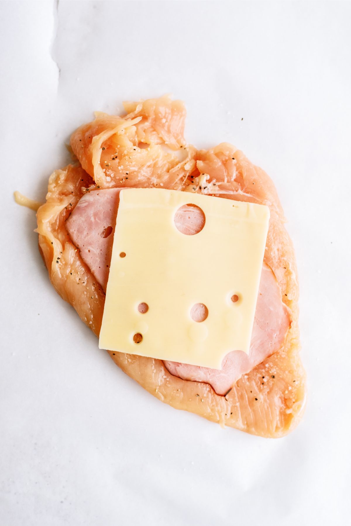 Slice of ham and a slice of cheese on top of a flattened chicken breast
