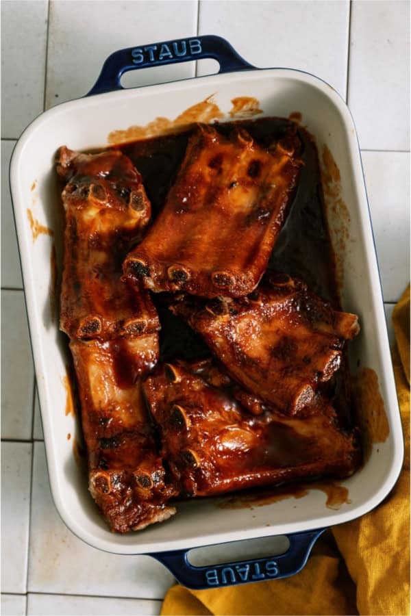 Oven Baked BBQ Ribs in a baking dish covered in BBQ sauce.