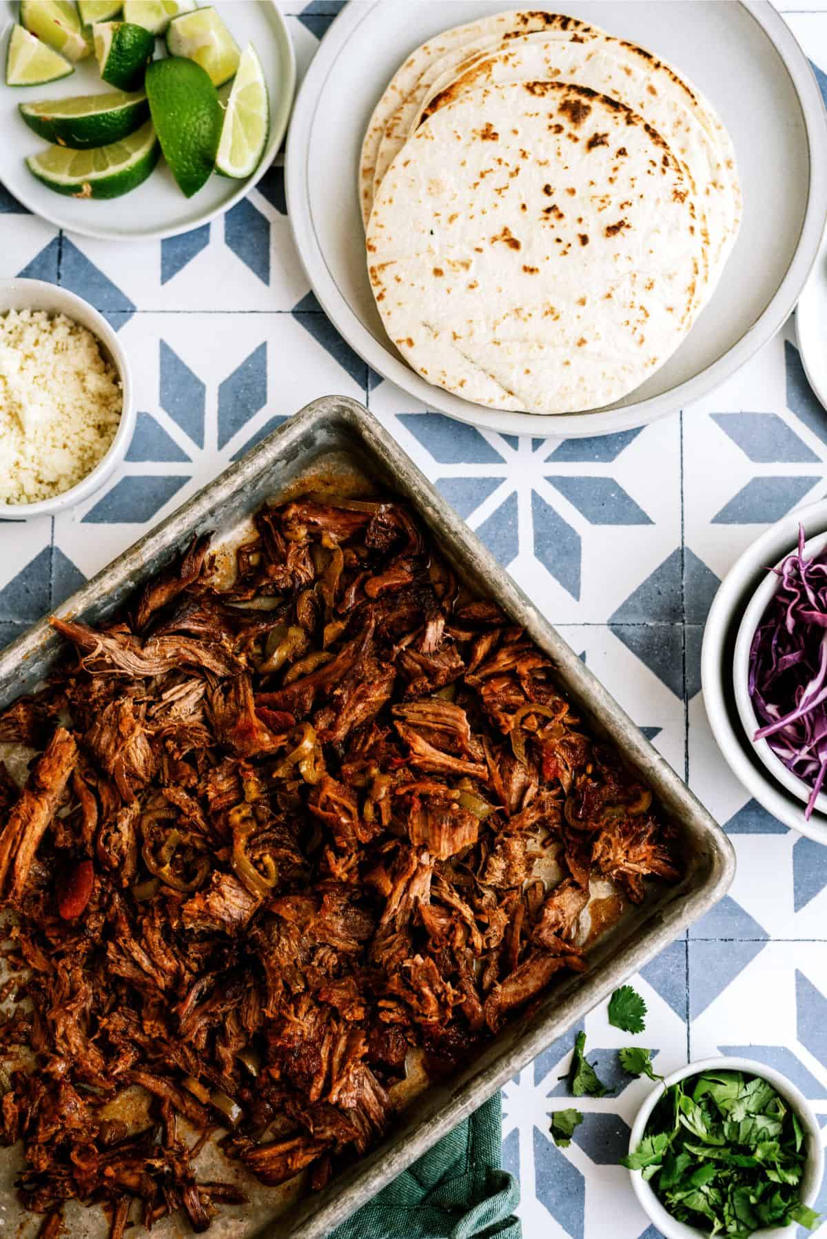 Slow Cooker Beef Carnitas meat on a pan surrounded by ingredients