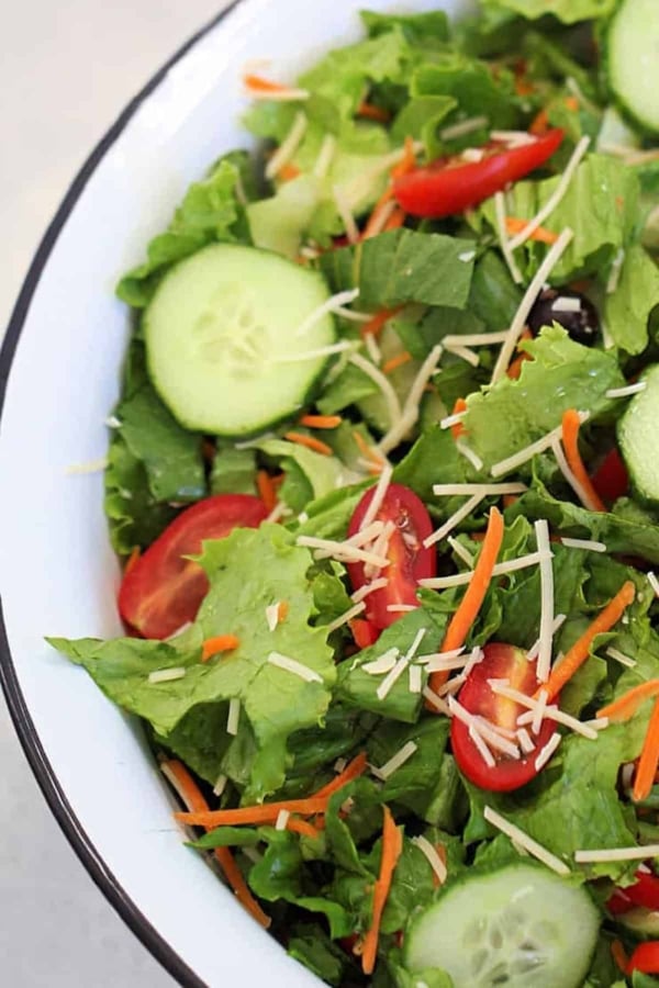 A bowl of salad containing lettuce, cucumber slices, cherry tomato halves, shredded carrots, and grated cheese.