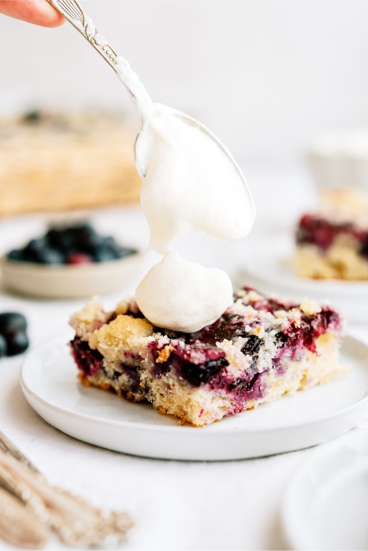 Placing a dollop of whipped topping on top of a square of Blueberry Coffee Cake