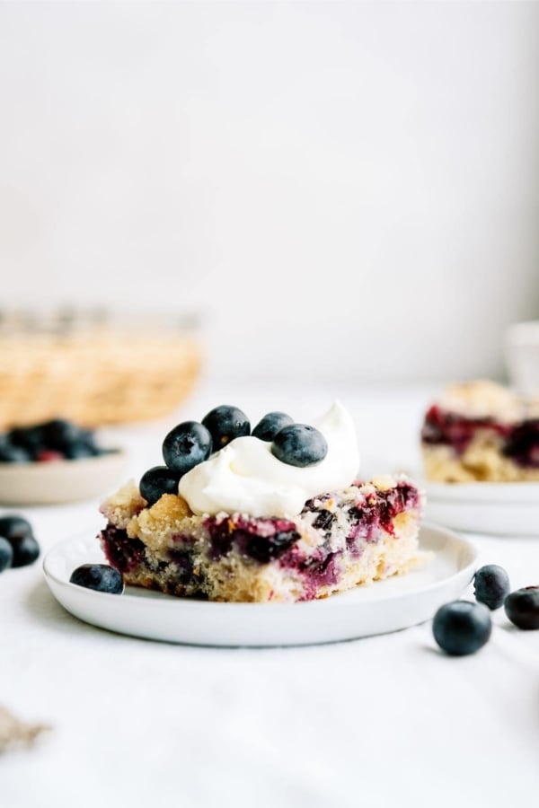 Blueberry coffee cake with whipped topping and fresh blueberries on a plate.