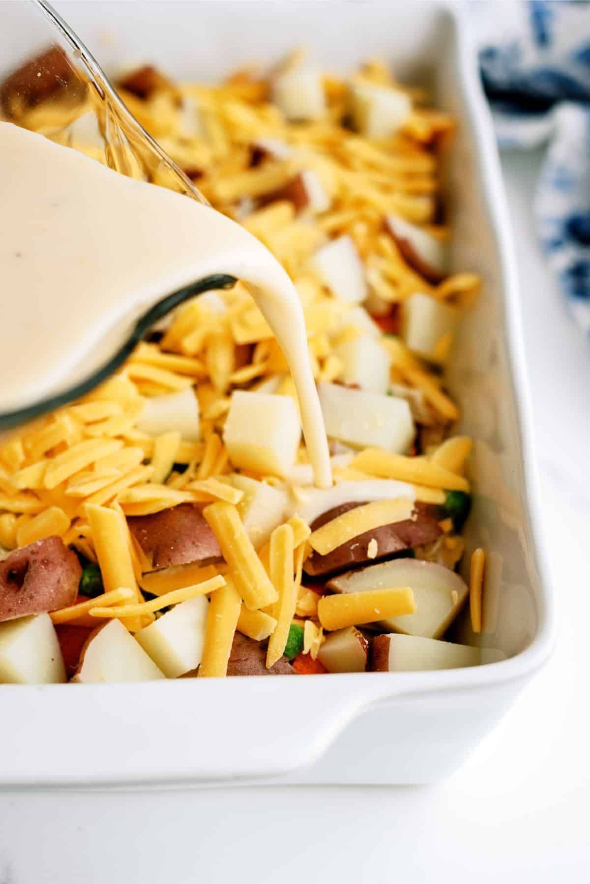 Pouring cheese sauce on top of ingredients in casserole dish