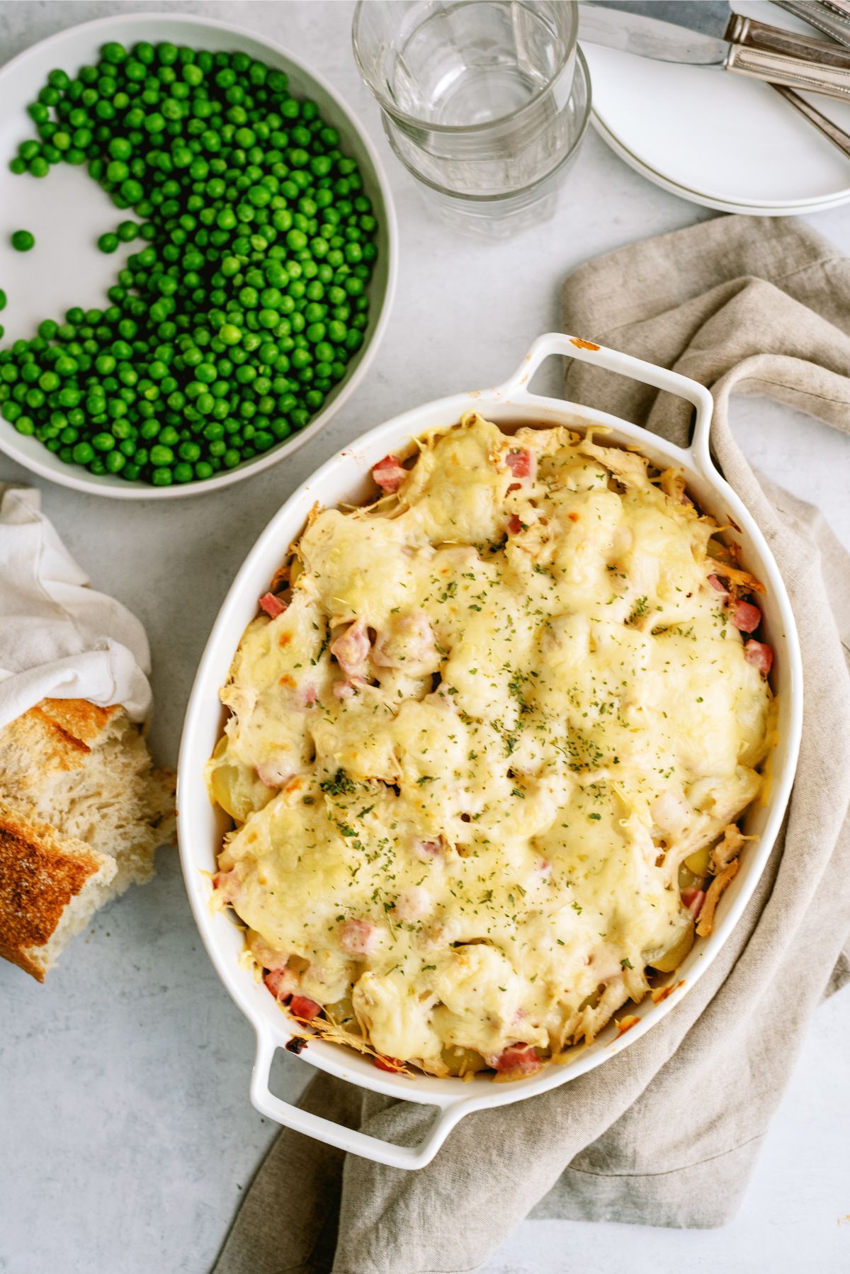 Chicken Cordon Bleu and Potatoes Casserole in a casserole dish with peas on the side