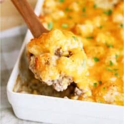 Cowboy Casserole in a large white casserole dish with a wooden spoon lifting out a scoop.