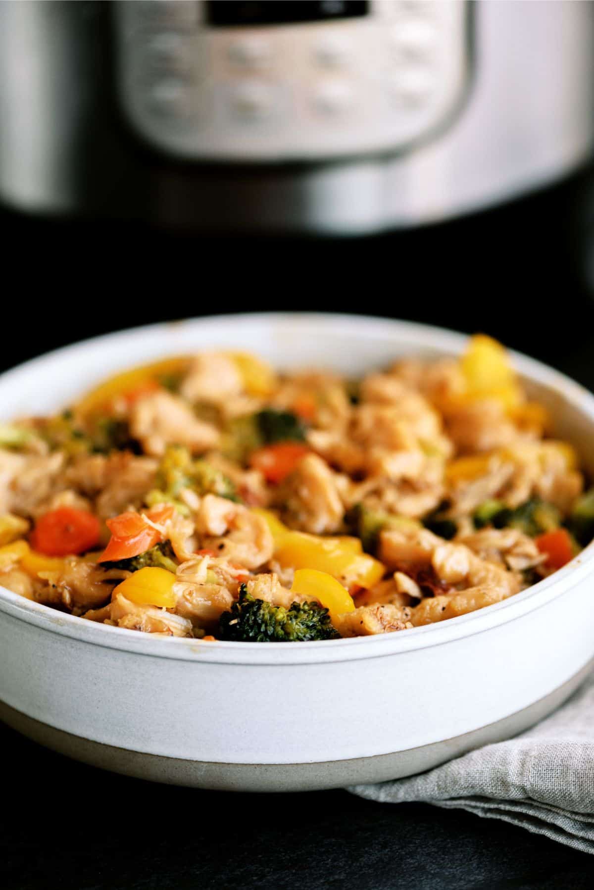 A bowl of Instant Pot Chicken and Veggie Stir Fry with an Instant Pot on the background