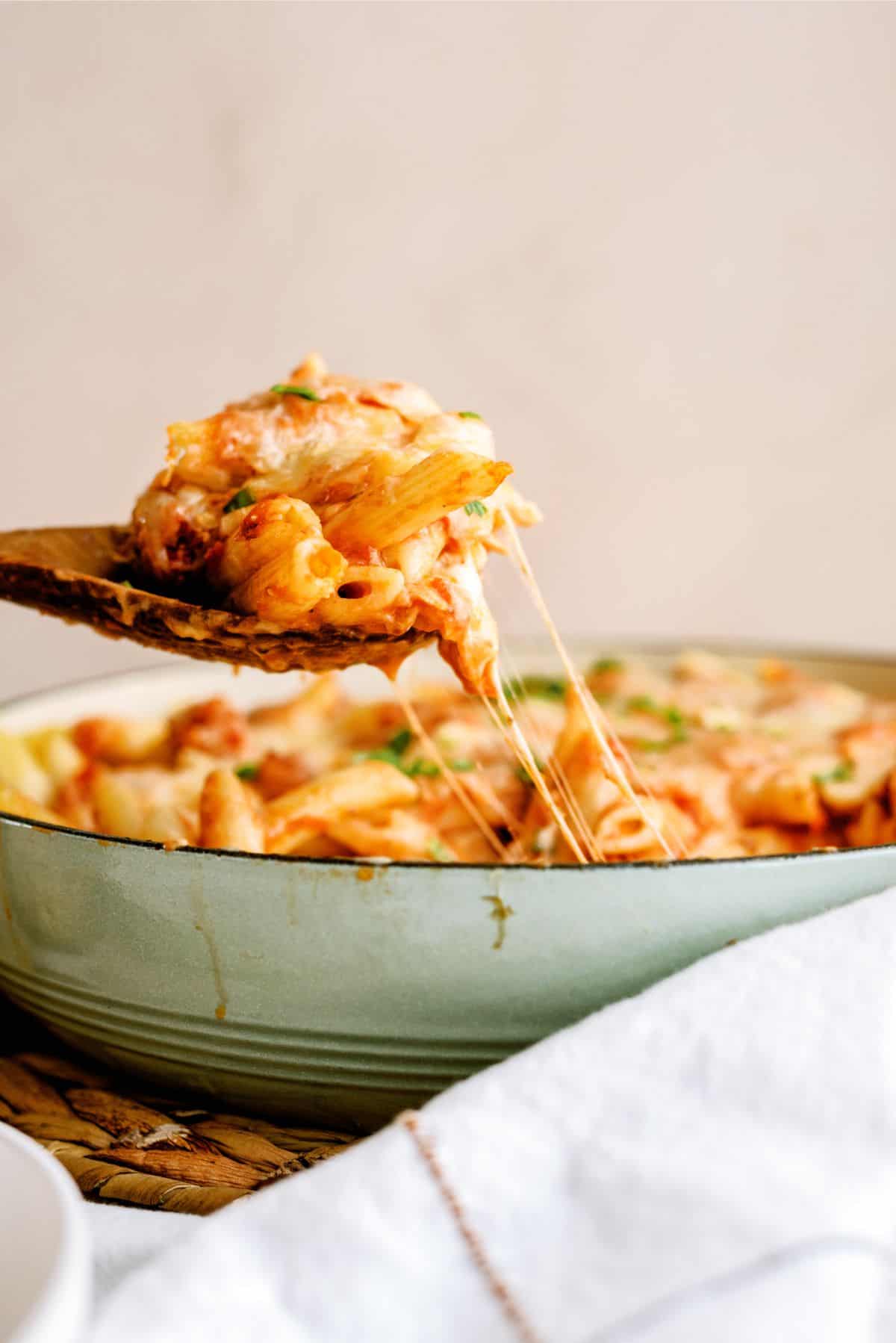 A wooden spoon holding a serving of Pink Sauce Chicken Pasta Bake being taken out of the baking dish