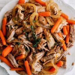 A plate of shredded pot roast topped with cooked onions, baby carrots, and sprigs of fresh thyme on a white dish.