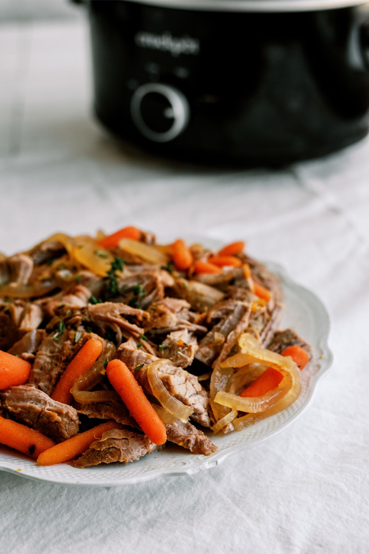 Slow Cooker Apricot Glazed Pork shredded on a plate with a slow cooker in the background