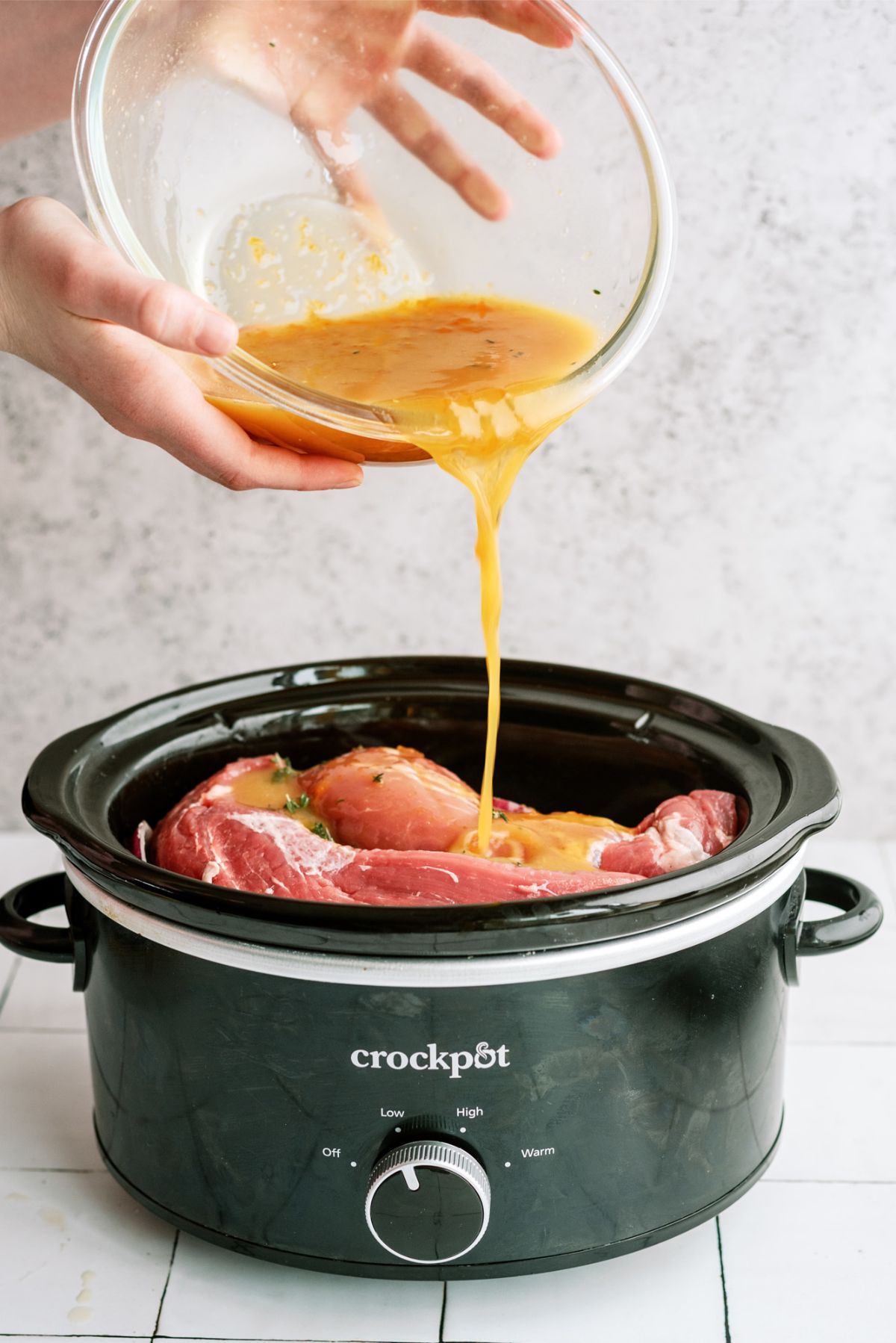 Pouring glaze over pork and veggies in the slow cooker