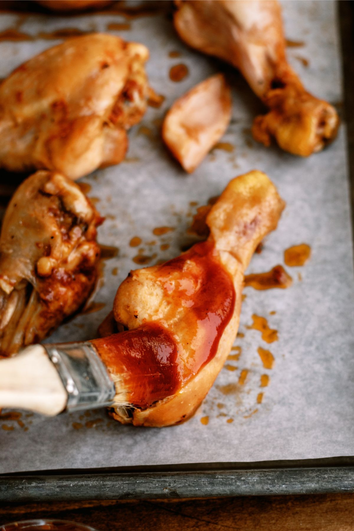A brush with BBQ sauce basting chicken drumsticks on a baking sheet
