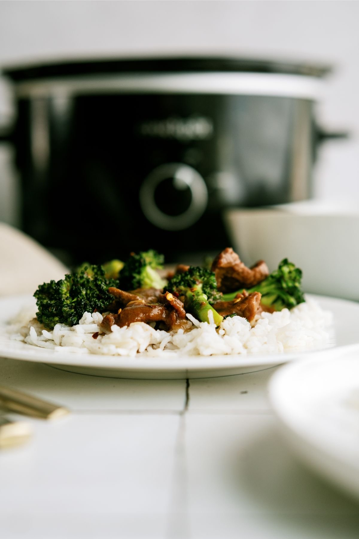 Slow Cooker Beef and Broccoli on a plate with the slow cooker in the background