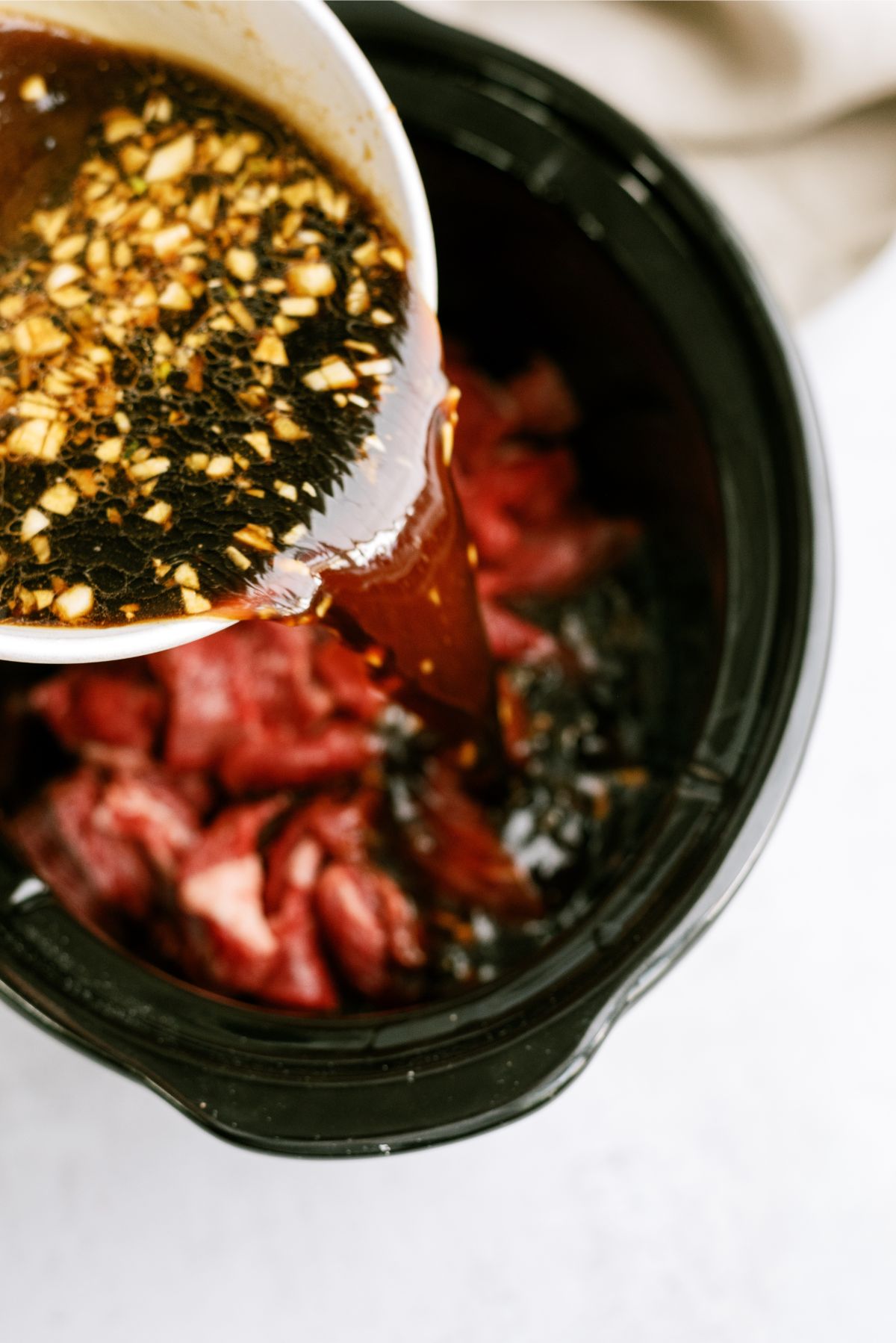 Pouring sauce over beef in slow cooker