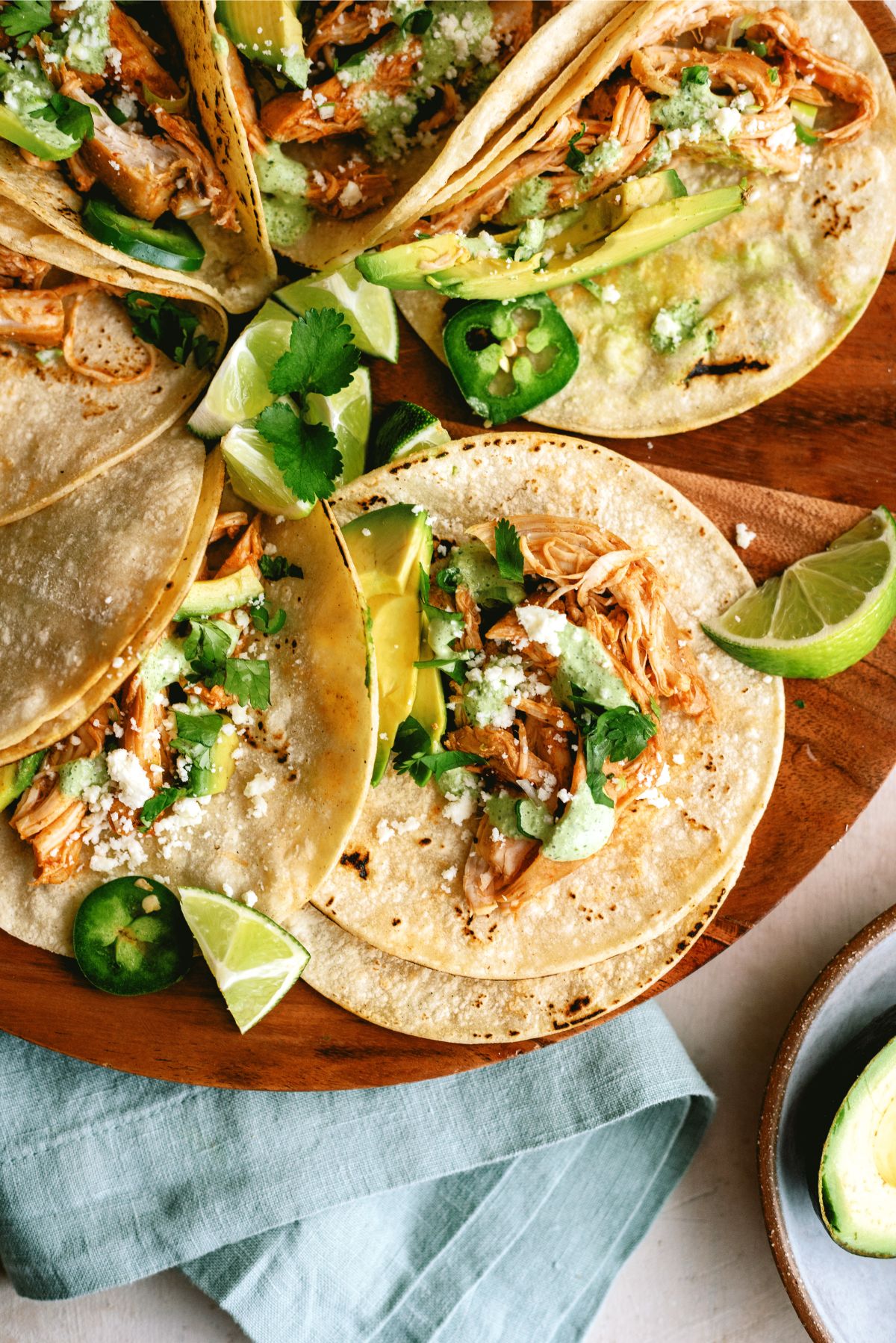 Slow Cooker Chicken Tinga Tacos topped with crema sauce, avocado and cheese with a lime wedge on the side