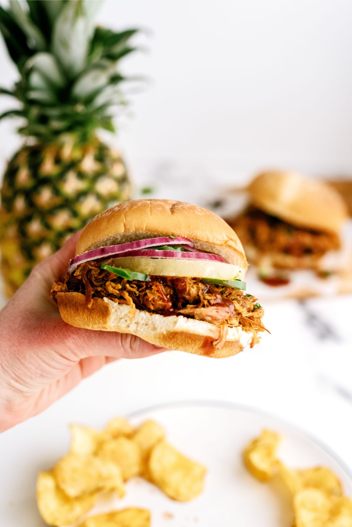 A hand holding a Slow Cooker Pineapple Pulled Pork Sandwich with a bite missing