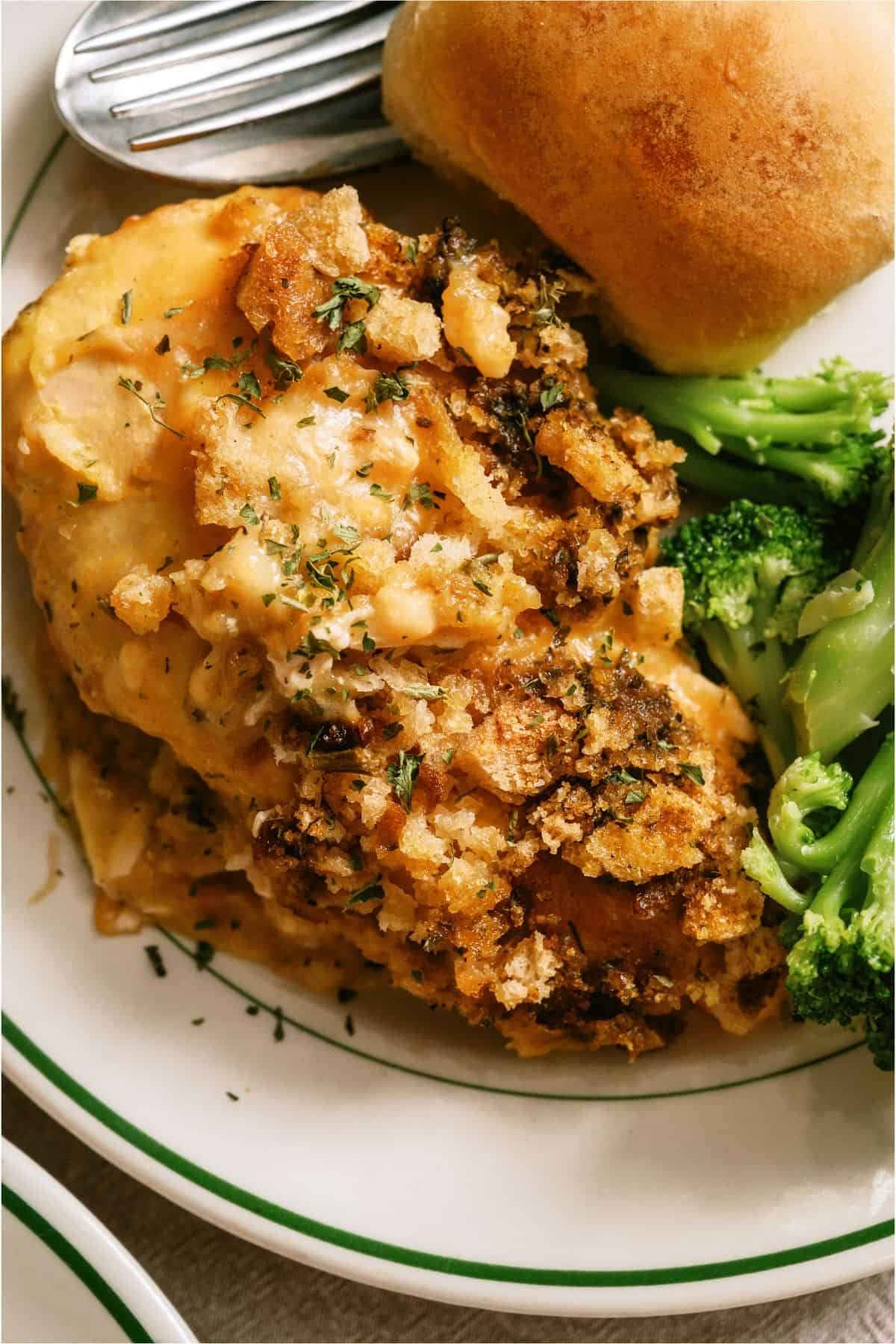 A serving of Slow Cooker Swiss Chicken on a plate with broccoli and rolls.