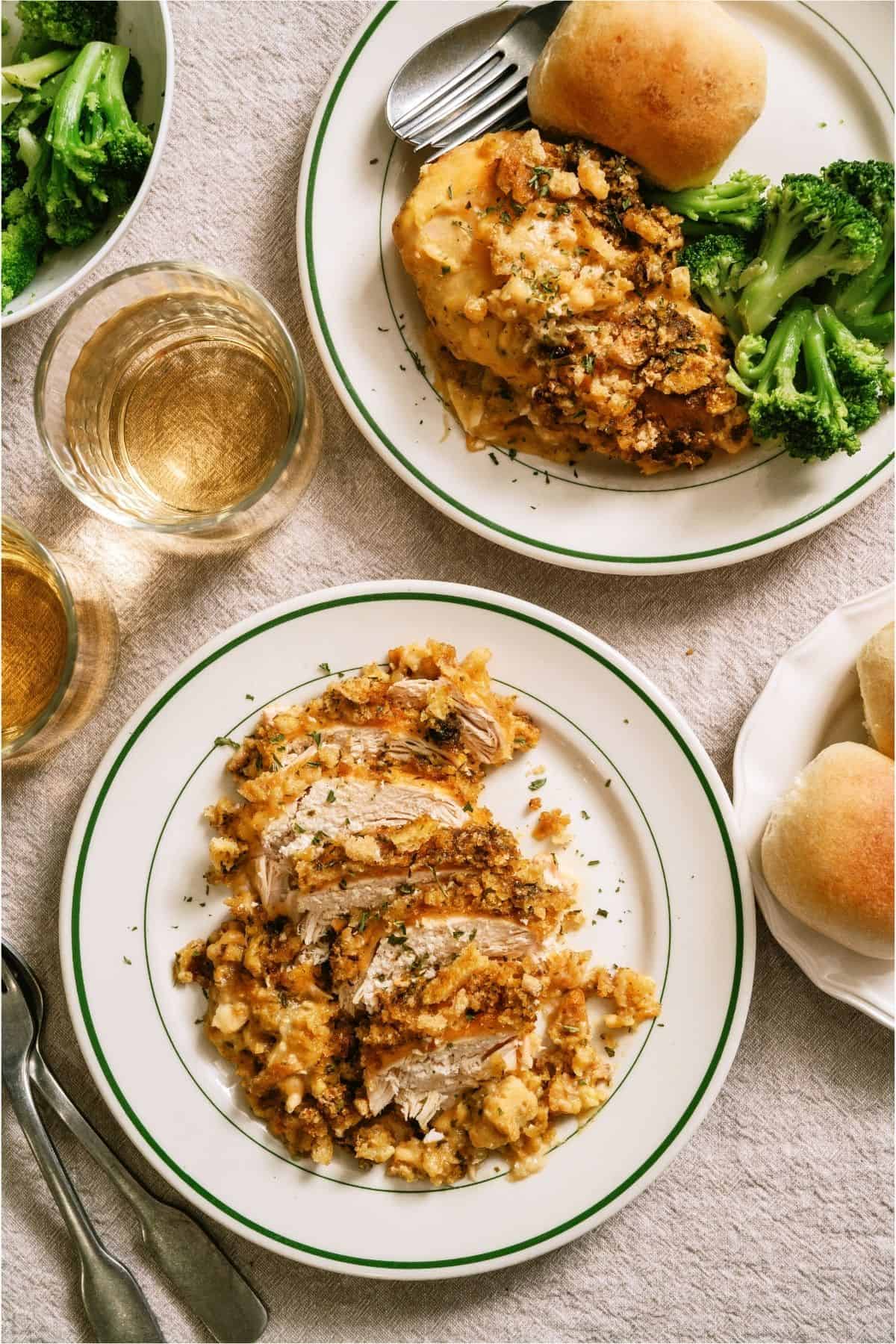 Two plates with servings of Slow Cooker Swiss Chicken, broccoli and rolls.
