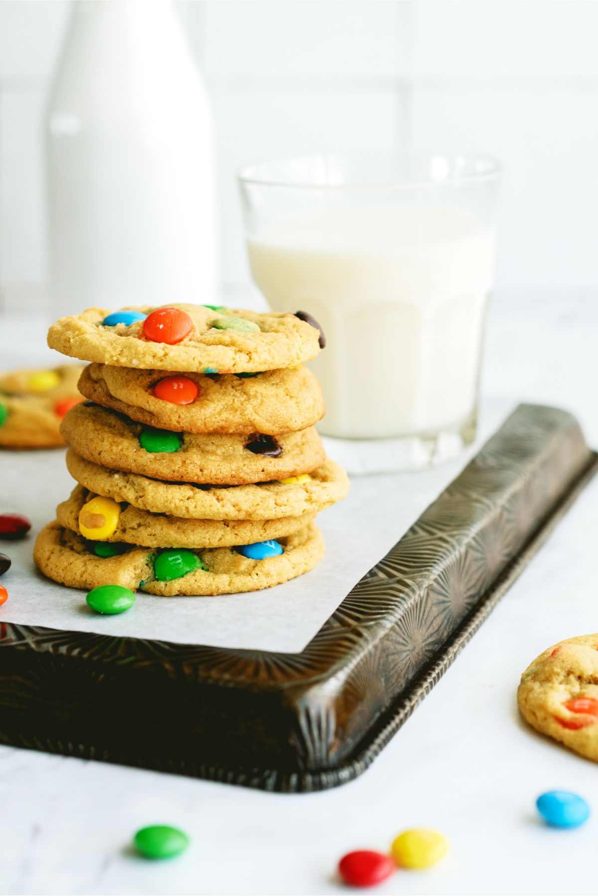 Chewy M&M Cookies stacked on a pan with a glass of milk