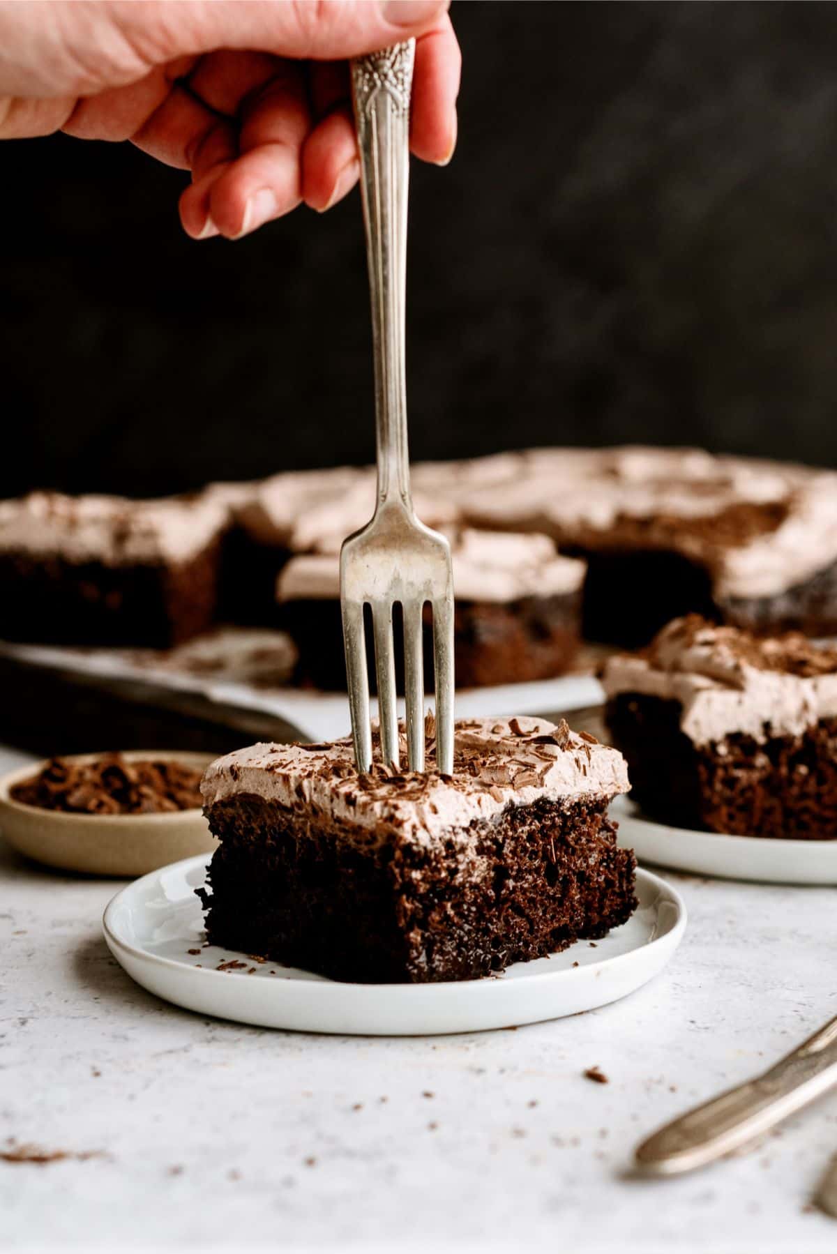 A slice of Hot Fudge Chocolate Poke Cake on a plate with a fork in the center of it