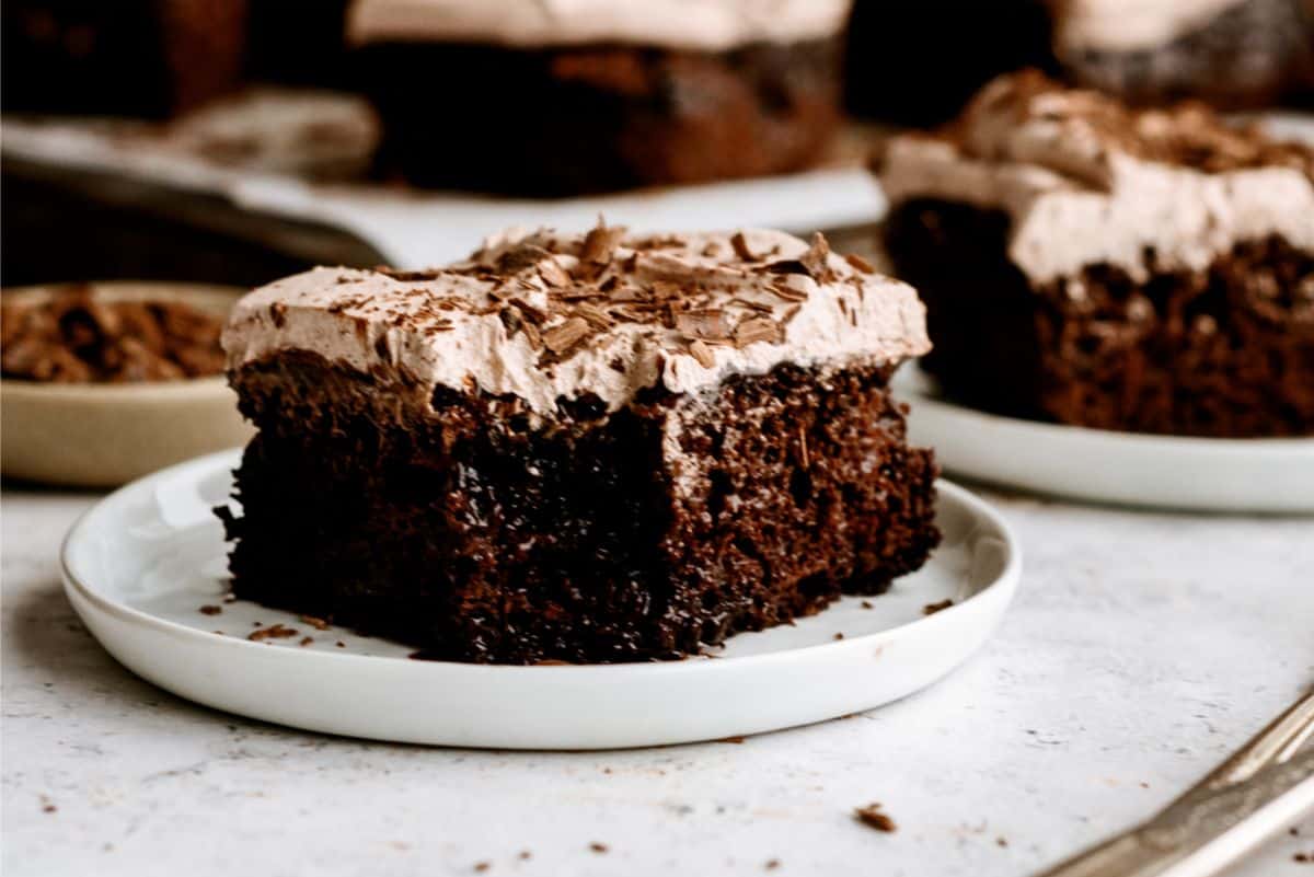 A slice of Hot Fudge Chocolate Poke Cake on a plate with a bite missing