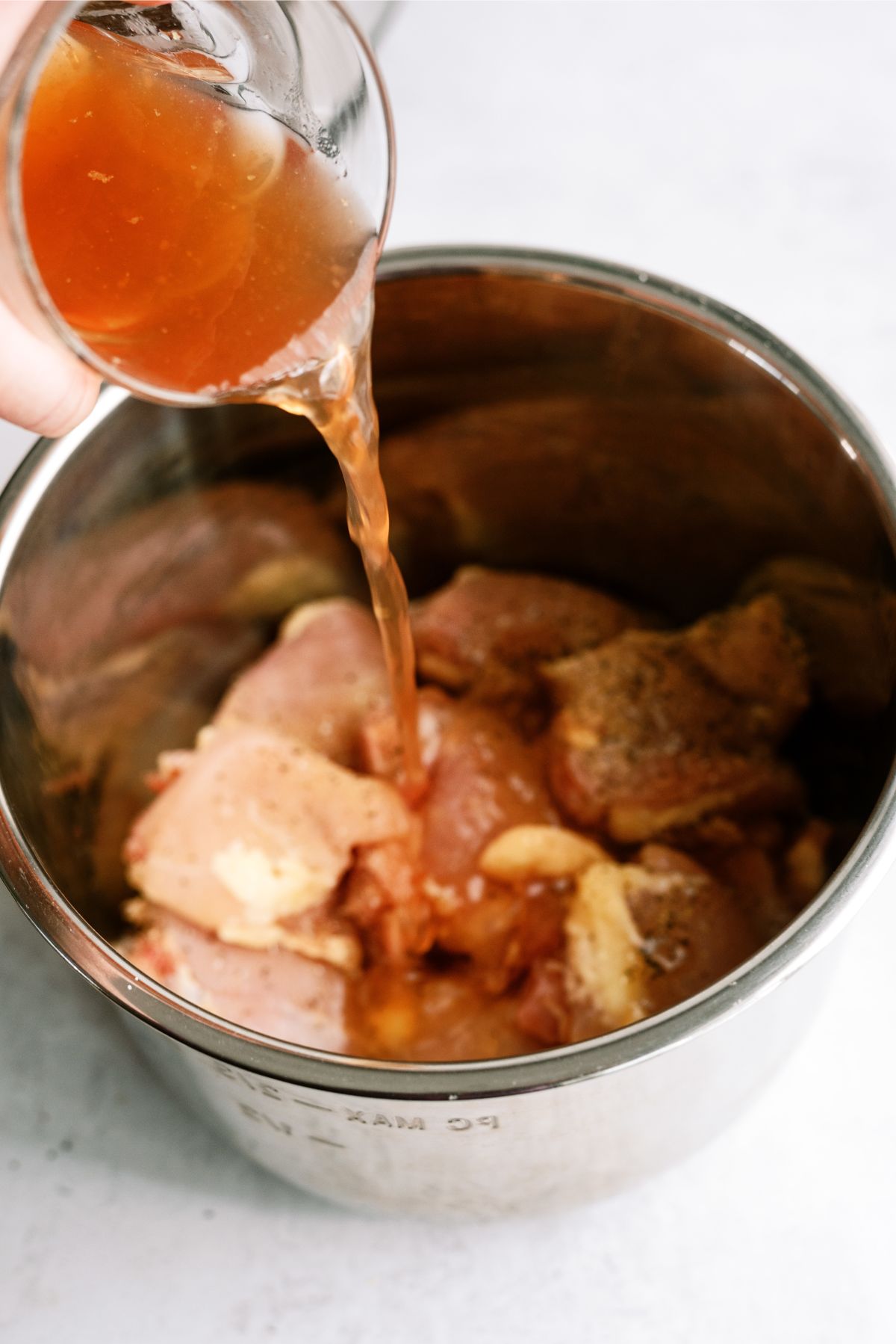 Pouring chicken broth on top of chicken thighs in Instant Pot