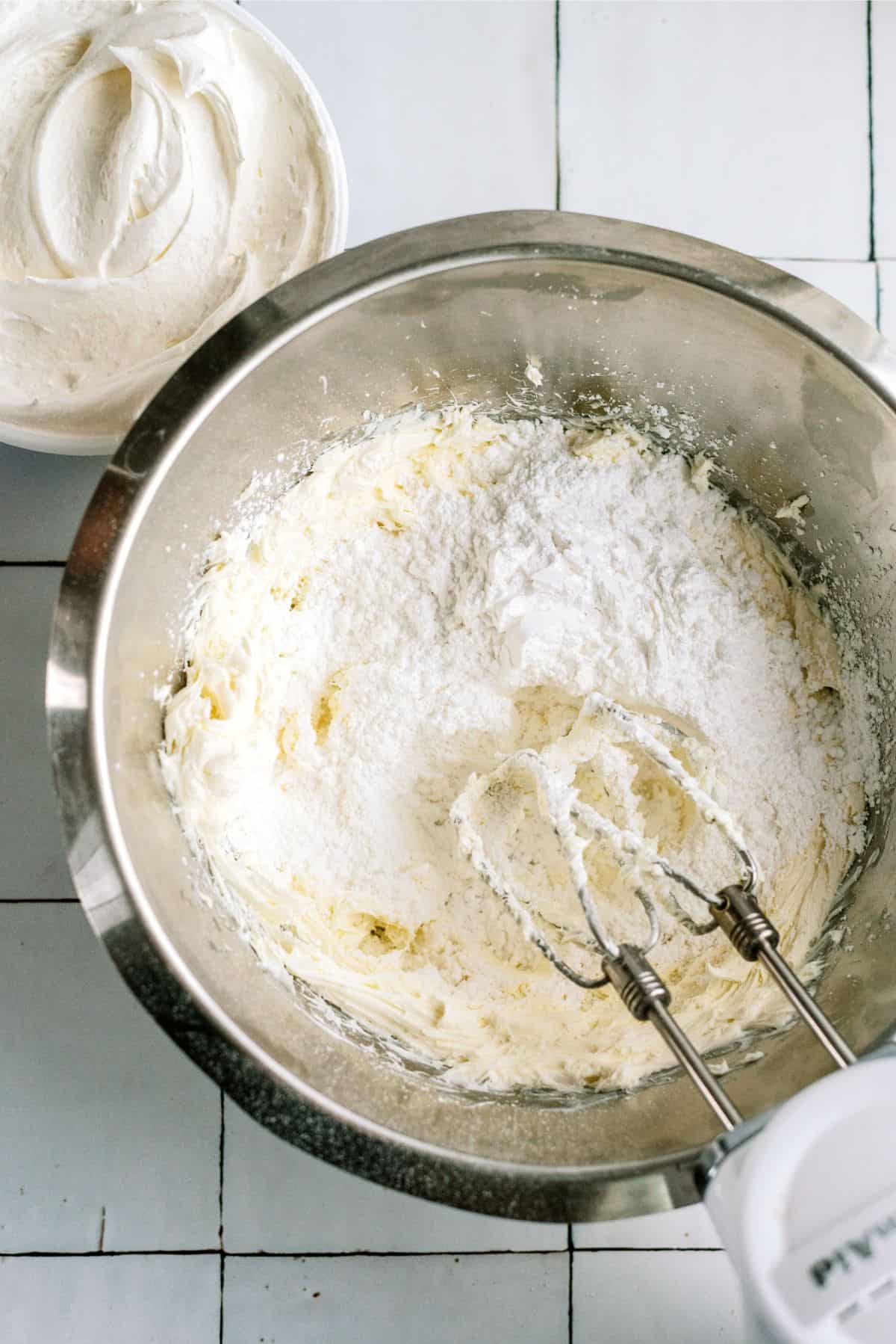 Cool whip layer ingredients in a mixing bowl with a hand mixer