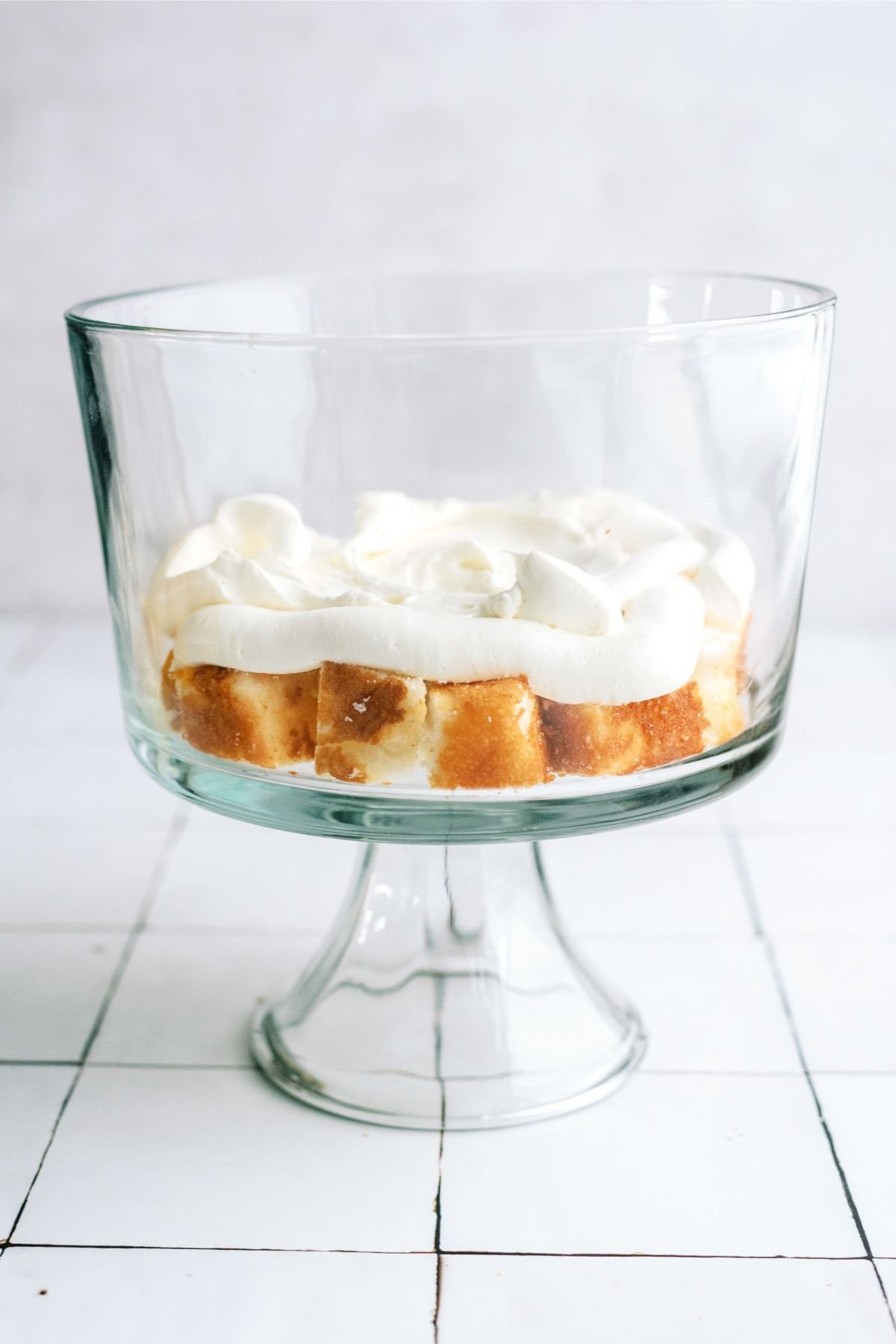 Cake cut into cubes in the bottom of a trifle bowl with half of the cream cheese mixture on top