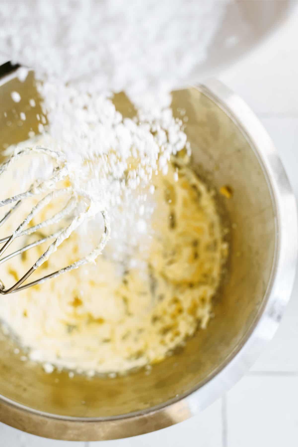 Adding powdered sugar to frosting mixture in bowl