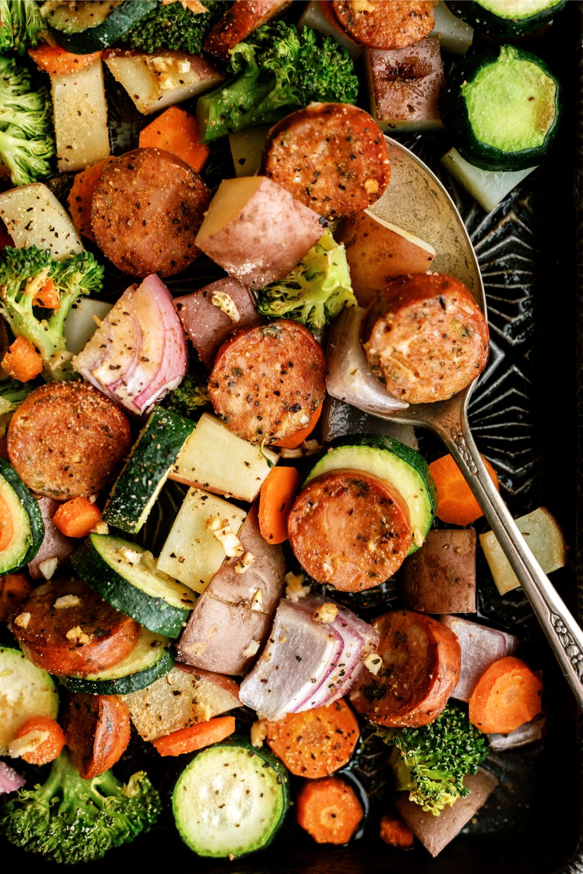 Close up of One Pan Garlic Sausage and Vegetables on a sheet pan with a spoon