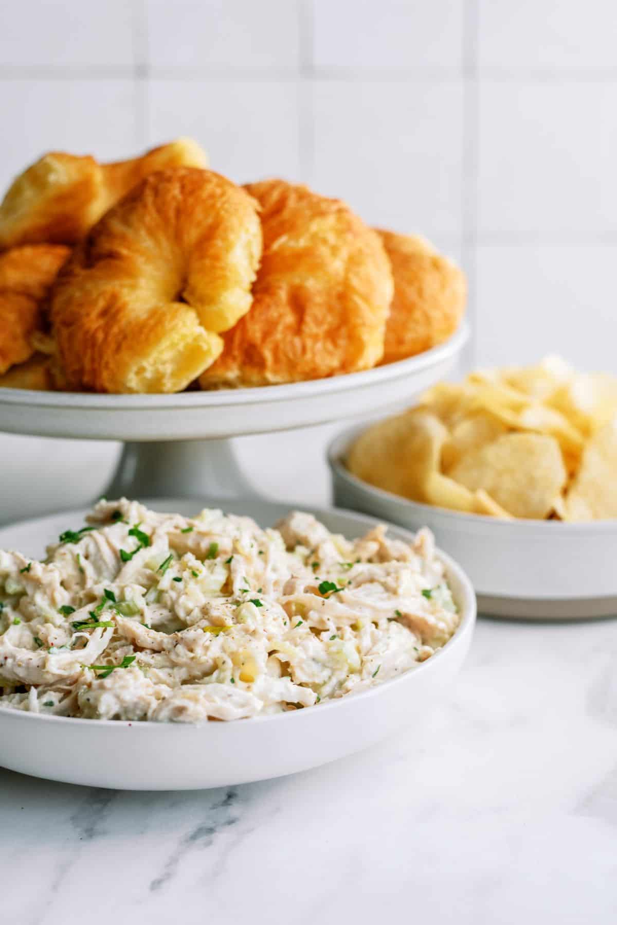 Pineapple Chicken Salad in a bowl with croissants on a stand behind