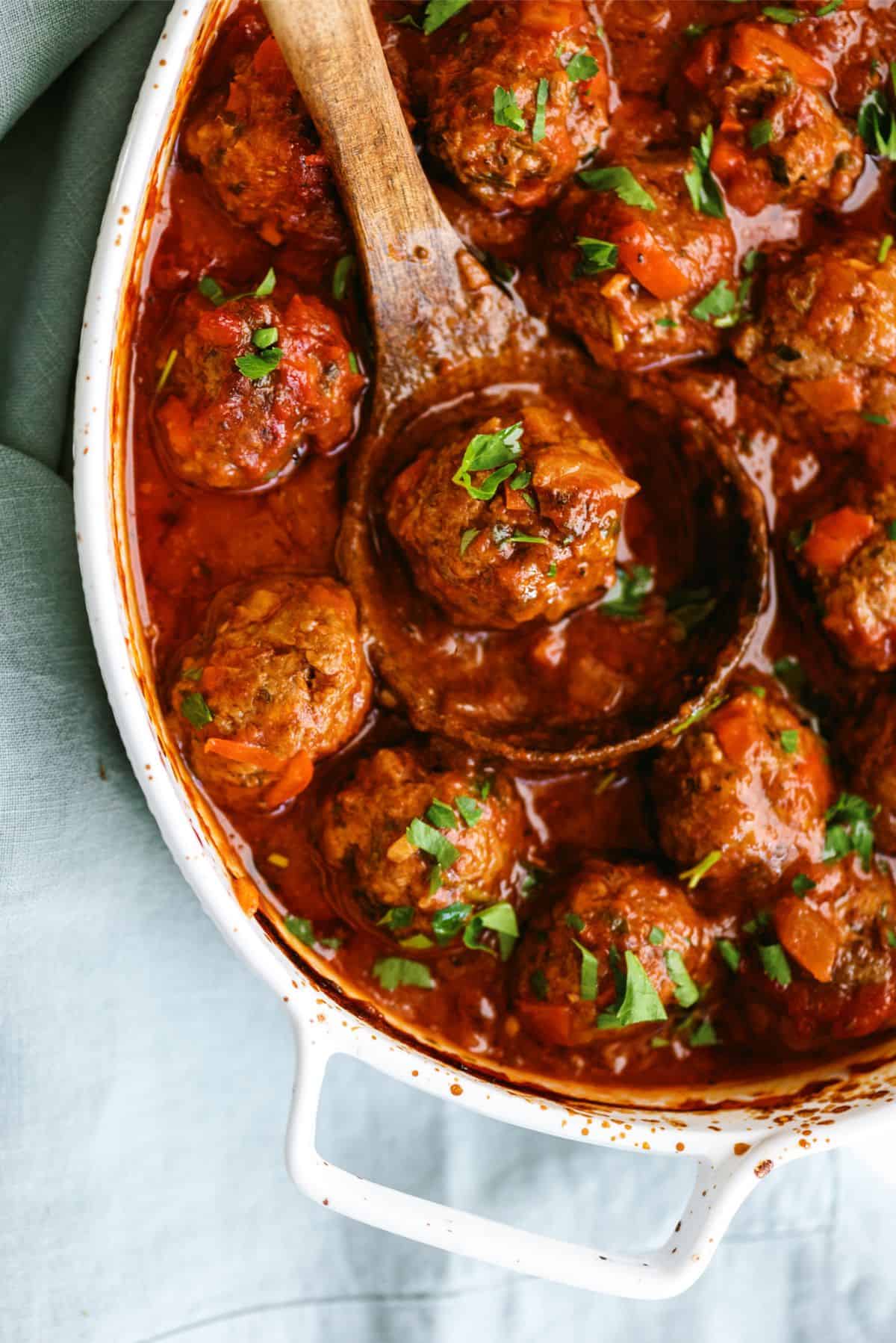 A serving bowl of Porcupine Meatballs with one being lifted out by a wooden spoon