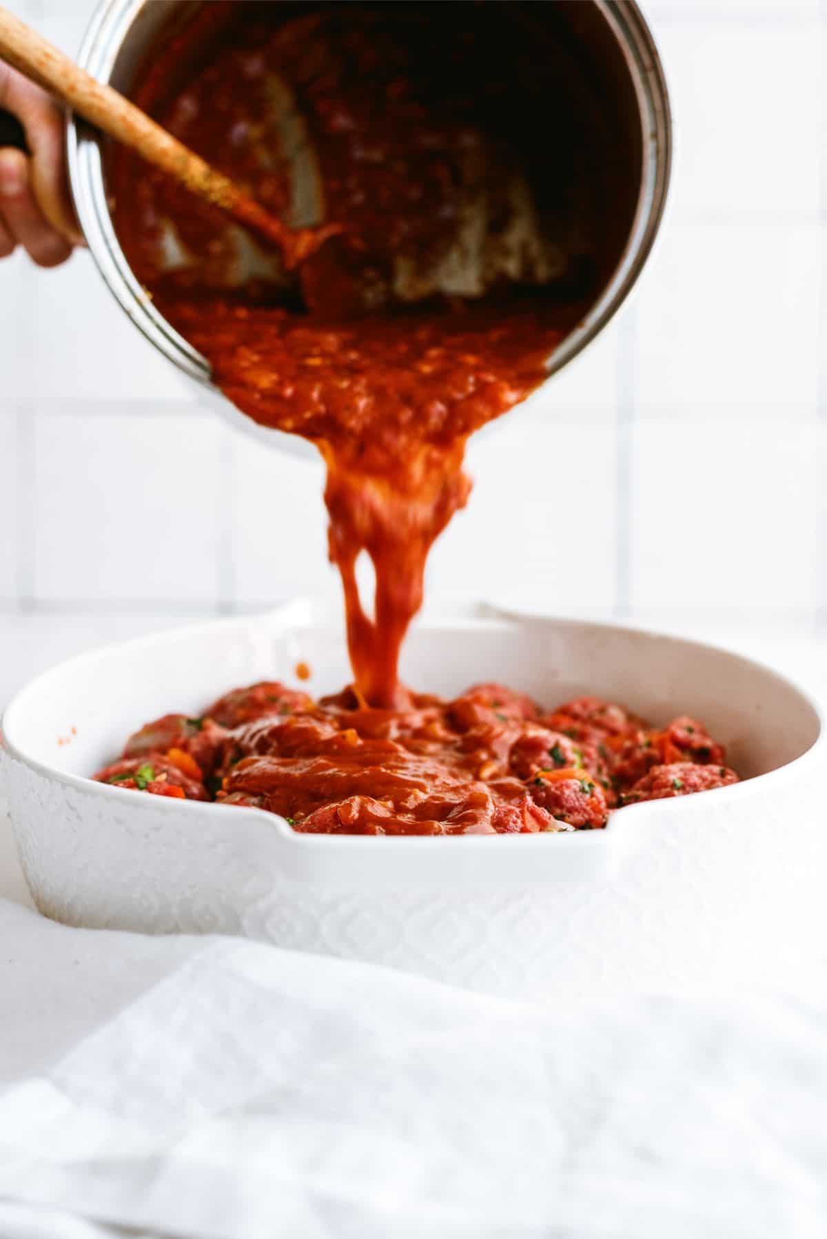 Pouring sauce from pan over Porcupine Meatballs in baking dish