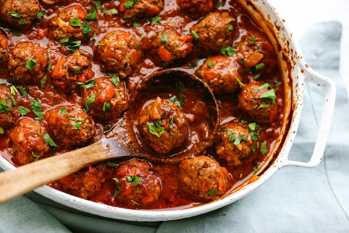 Porcupine Meatballs in baking dish with one meatball being lifted out with a wooden spoon