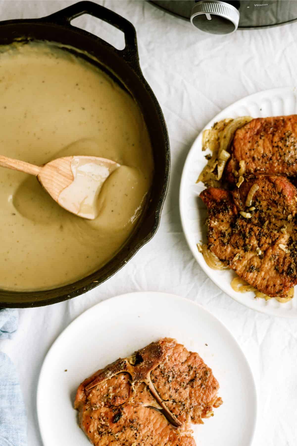 A skillet with gravy and a plate of pork chops cooked