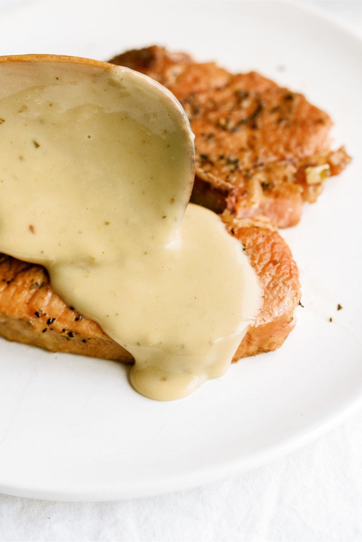 A spoon pouring gravy on top of cooked pork chops