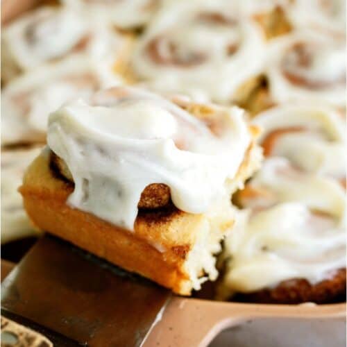 A pan of T Classic Cinnamon Rolls with a spatula lifting one out