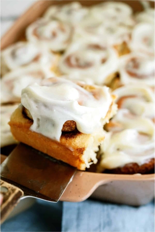 A pan of T Classic Cinnamon Rolls with a spatula lifting one out