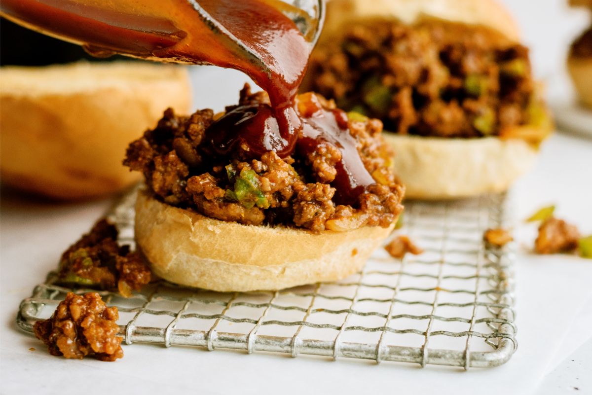 Pouring extra BBQ sauce on top of BBQ Sloppy Joe sandwich