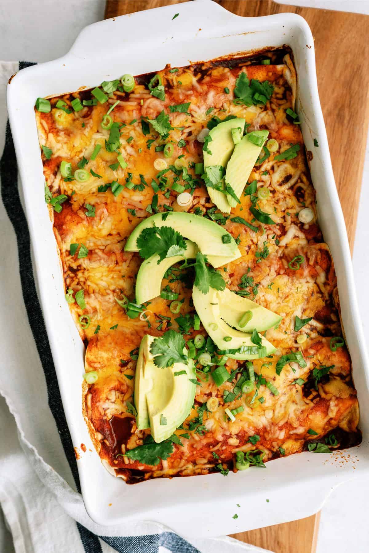 A pan full of Chicken Fiesta Enchiladas with sliced avocados on top