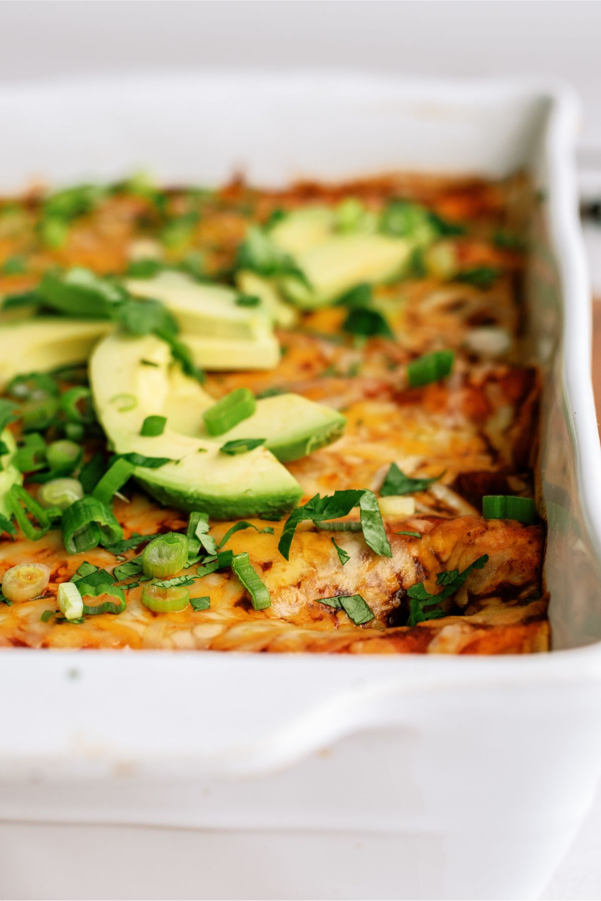 Side view of a pan of Chicken Fiesta Enchiladas with sliced avocados on top