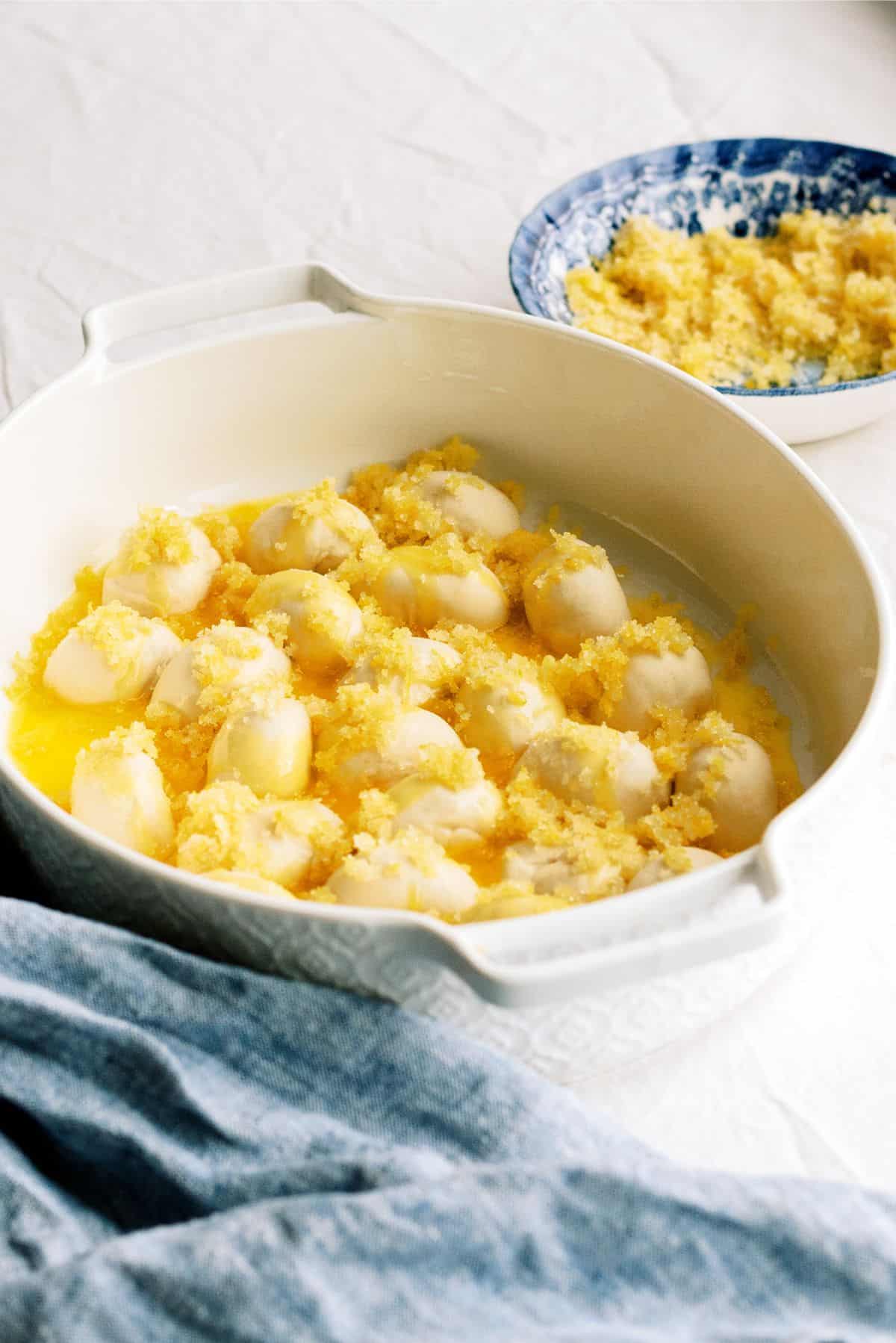 Rolls cut in half in a baking dish with butter and lemon sugar sprinkled on top