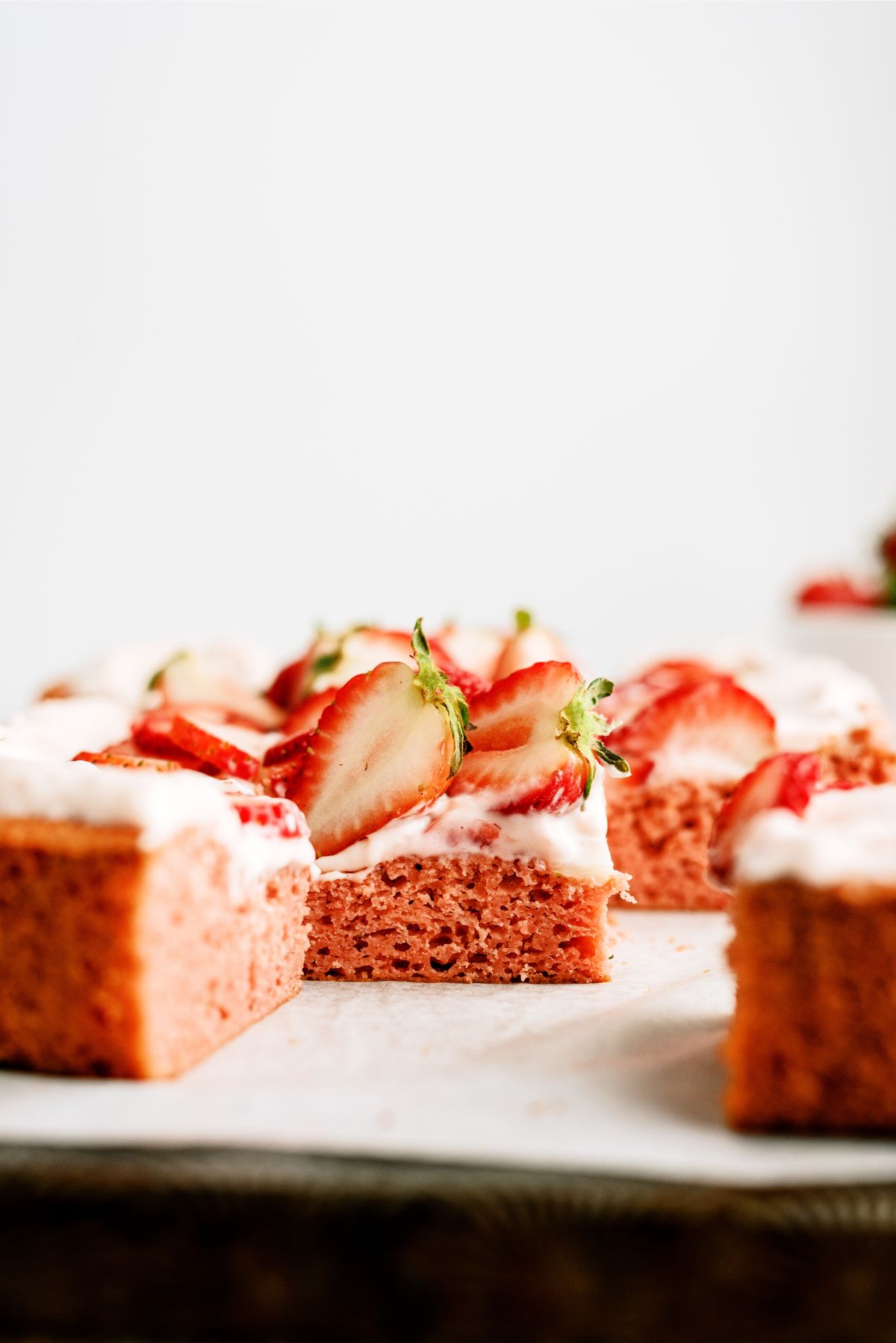 Frosted Strawberry Sheet Cake cut into squares with fresh strawberries on top